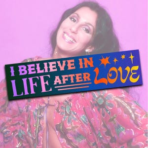 May include: A blue and green bumper sticker with the text "I Believe in Life After Love" in pink and orange letters. The sticker features a stylized heart and stars.
