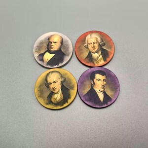Op de afbeelding: Vier ronde houten tokens met portretten van historische figuren. Elke token toont een ander persoon tegen een anders gekleurde achtergrond. De tokens zijn ongeveer 5 cm in diameter.