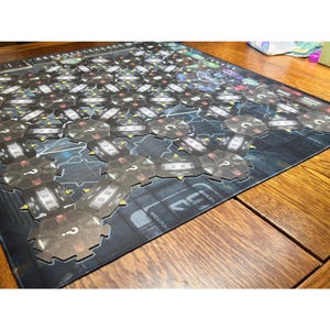 May include: A board game with a futuristic design. The game board is dark with a grid of hexagonal tiles. Each tile has a question mark and a detailed design. The game is set on a wooden table.