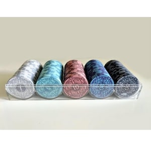 Op de afbeelding: Een set van zes stapels pokerchips in een transparante acryl tray. De chips zijn in vier kleuren: grijs, blauw, rood en zwart. Elke stapel heeft een ander nummer op de bovenste chip: 1, 5, 10 en 25.