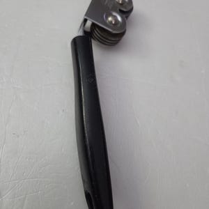 May include: A can opener with a black handle and a silver metal cutting mechanism. The opener has a curved handle for grip and a wheel for cutting. The can opener is designed for opening cans.