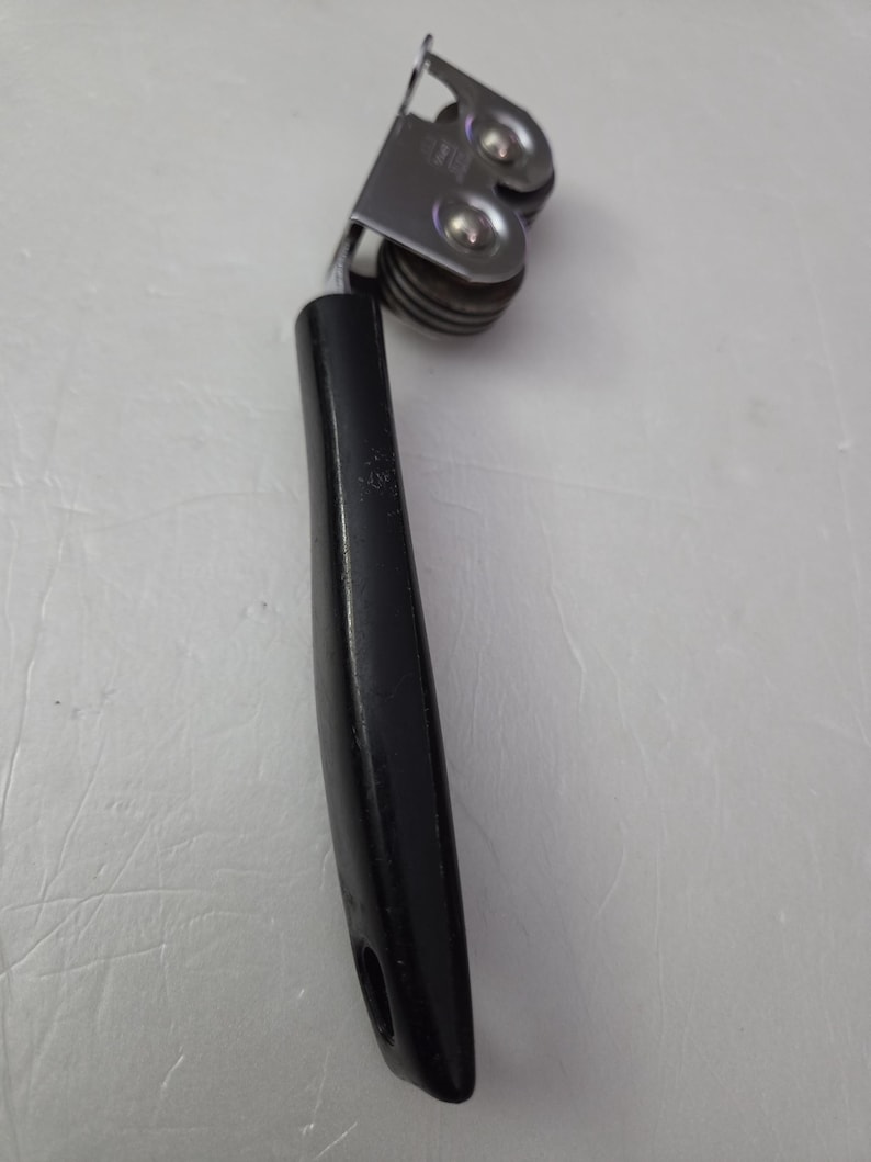 May include: A can opener with a black handle and a silver metal cutting mechanism. The opener has a curved handle for grip and a wheel for cutting. The can opener is designed for opening cans.