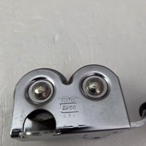 May include: A chrome-plated can opener with the text "EKCO USA". The can opener has two circular components with rivets and a handle. The can opener is designed to open cans.