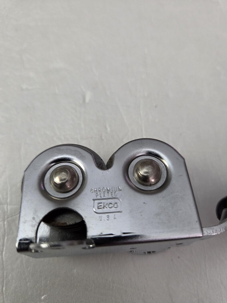 May include: A chrome-plated can opener with the text "EKCO USA". The can opener has two circular components with rivets and a handle. The can opener is designed to open cans.