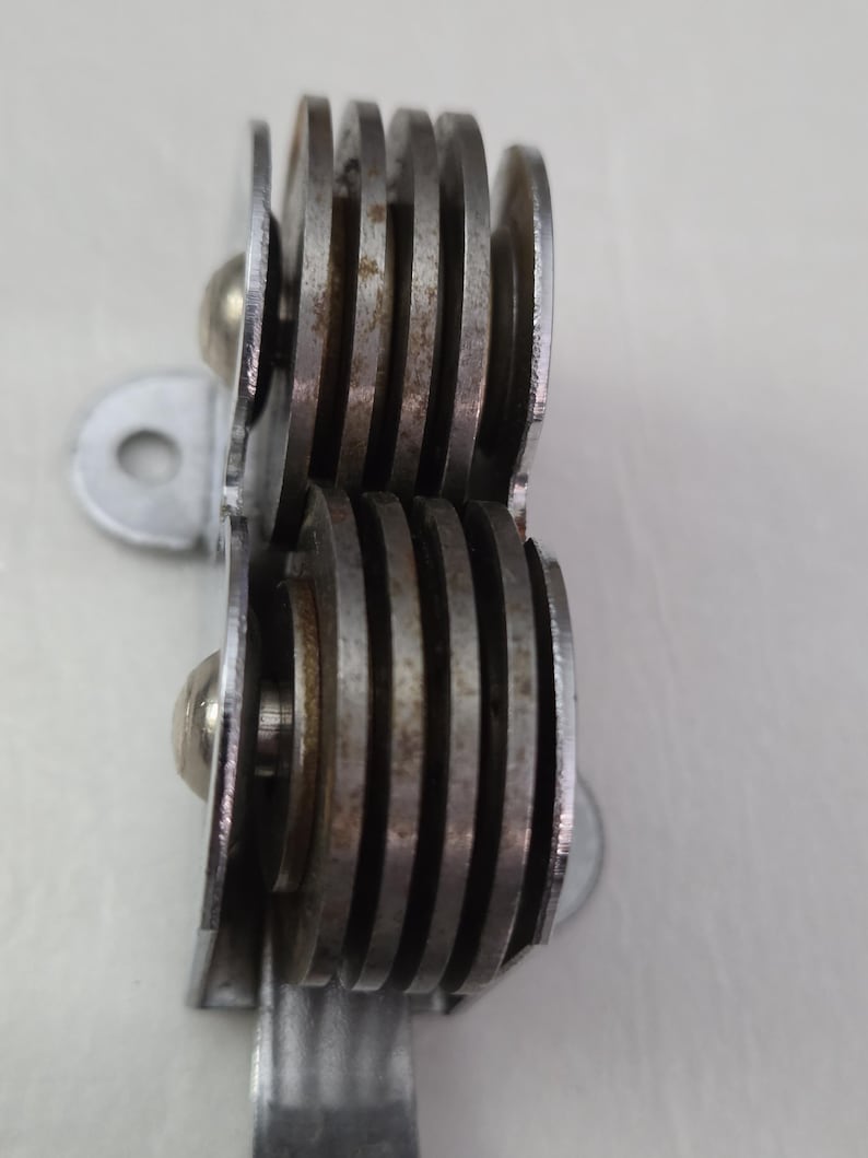 May include: Close-up of a vintage metal can opener. The can opener has a series of circular blades and a silver handle. The blades are stacked and show signs of age and use. The design is simple and functional.
