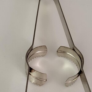 Puede incluir: Un pelador de c&iacute;tricos de acero inoxidable con un borde dentado. El pelador est&aacute; abierto y listo para usar.