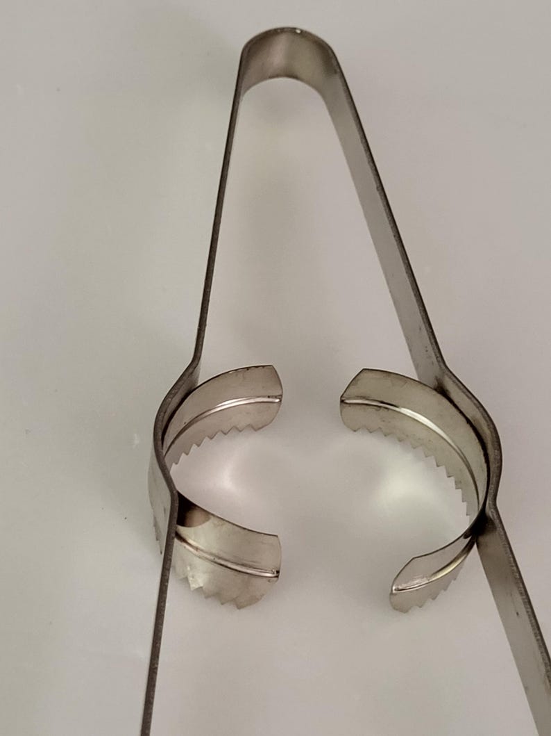 Puede incluir: Un pelador de c&iacute;tricos de acero inoxidable con un borde dentado. El pelador est&aacute; abierto y listo para usar.