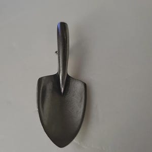 May include: A small, antique-style garden trowel with a dark, metallic finish. The trowel features a curved handle and a spade-shaped blade, ideal for planting and gardening tasks. The overall design suggests a vintage or rustic aesthetic.