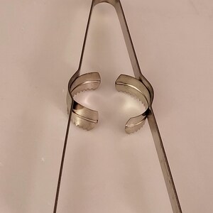 Puede incluir: Un cortador de huevos de metal plateado con dos anillos dentados y dos mangos largos.