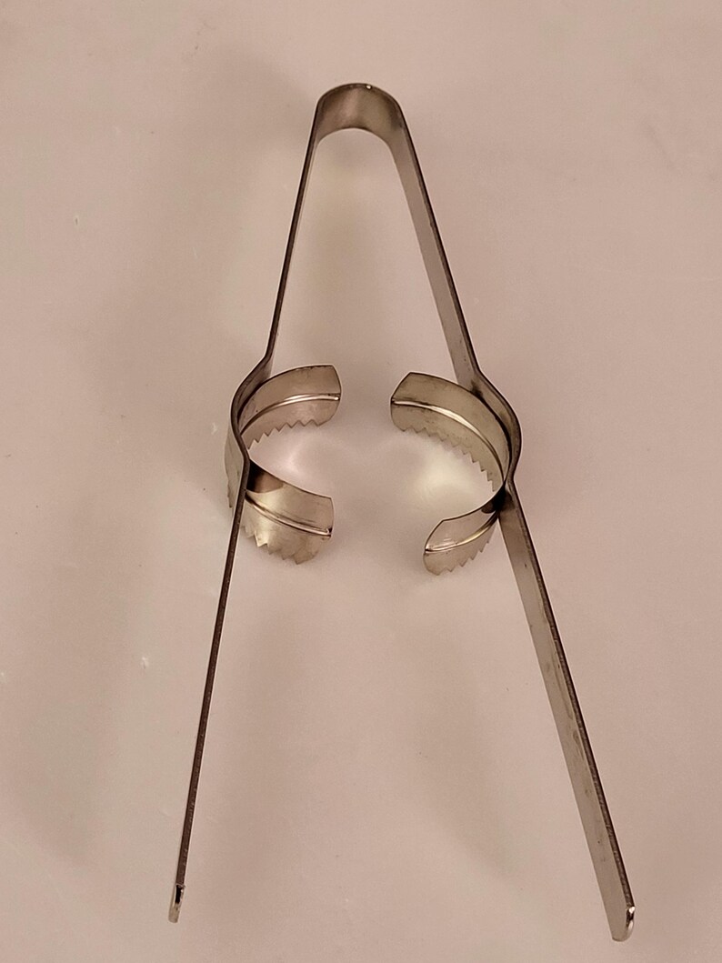 Puede incluir: Un cortador de huevos de metal plateado con dos anillos dentados y dos mangos largos.