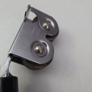 May include: Close-up of a vintage can opener. The can opener is made of shiny, silver-colored metal with a black handle. The design includes a cutting wheel and a lever for opening cans. The can opener is a kitchen utensil.