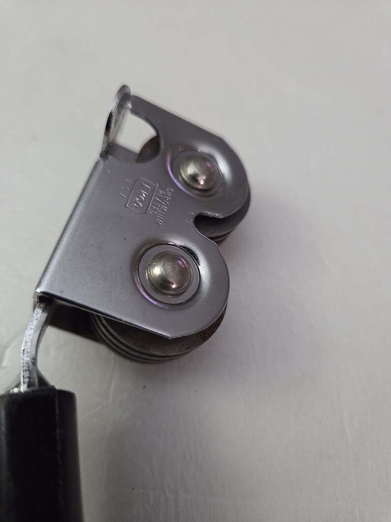 May include: Close-up of a vintage can opener. The can opener is made of shiny, silver-colored metal with a black handle. The design includes a cutting wheel and a lever for opening cans. The can opener is a kitchen utensil.