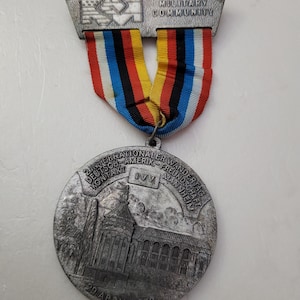 May include: A silver medal with a colorful ribbon. The medal has text that reads "MANNHEIM MILITARY COMMUNITY" and "29 APRIL 1979". The ribbon is striped with red, white, blue, and yellow.