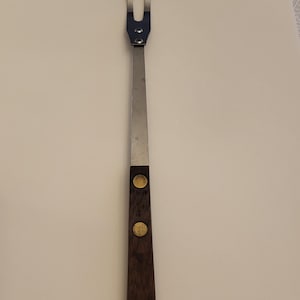 May include: A stainless steel grilling fork with a wooden handle and two gold accents.