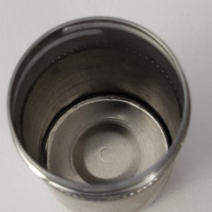 May include: A stainless steel cup with a smooth, shiny finish. The cup has a rounded bottom and a slightly flared top.
