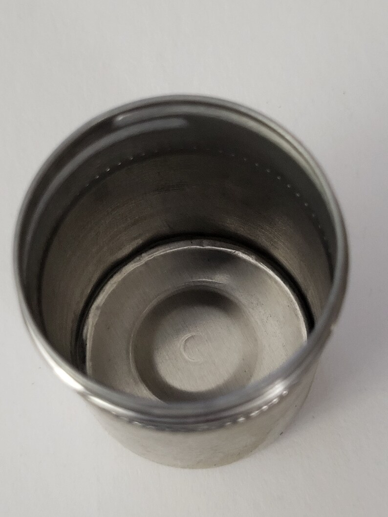 May include: A stainless steel cup with a smooth, shiny finish. The cup has a rounded bottom and a slightly flared top.