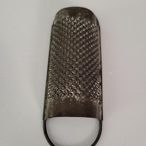 May include: A silver metal grater with a small loop handle. The grater has a diamond-shaped pattern.