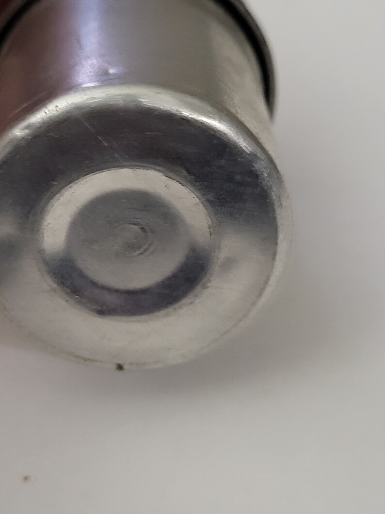 May include: Close-up of the bottom of a silver metal container. The container has a smooth, shiny surface.