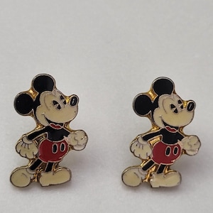May include: Pair of Mickey Mouse enamel pins. Each pin features Mickey Mouse in a walking pose, with black ears, a cream-colored face, red shorts, and white gloves. The pins have a gold-colored border.