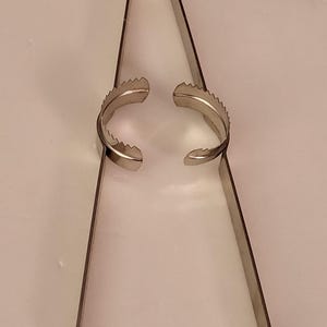 May include: Silver-toned metal tongs with serrated edges on the ends. The tongs are open and ready to grab something.