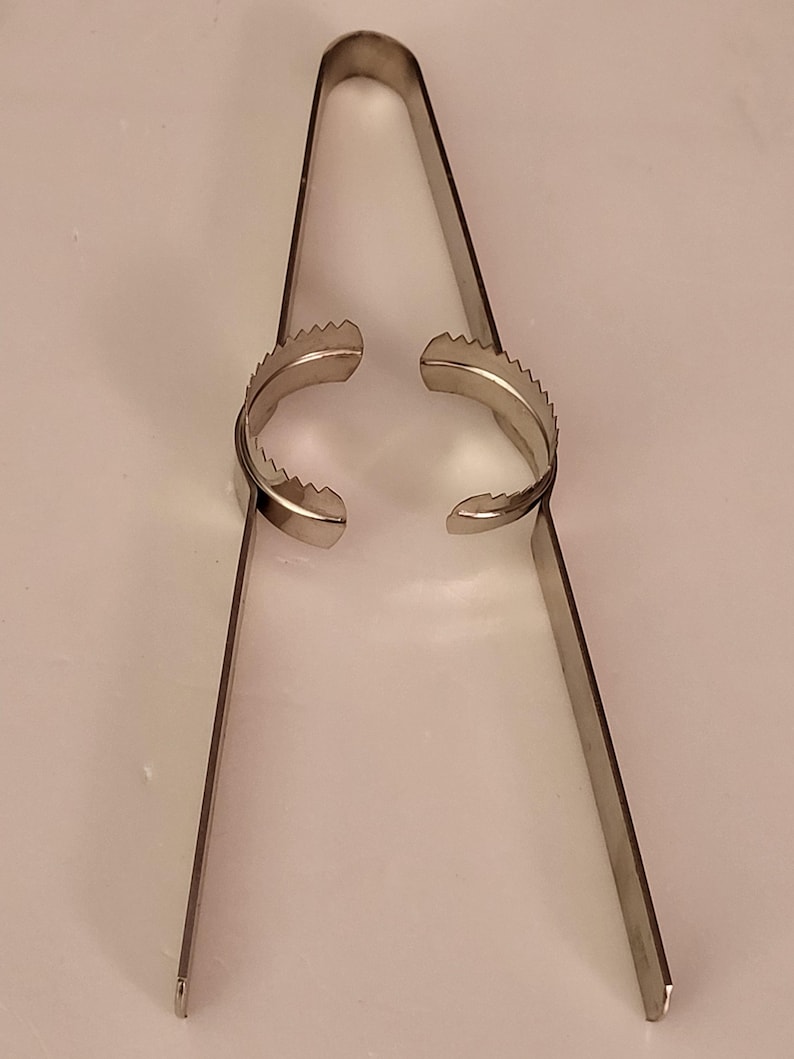 Puede incluir: Pinzas de metal plateadas con bordes dentados en los extremos. Las pinzas est&aacute;n abiertas y listas para agarrar algo.