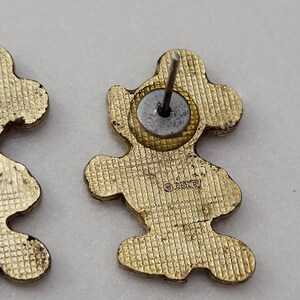 May include: Gold-toned Mickey Mouse stud earrings. The earrings are in the shape of Mickey Mouse with a textured surface. The back of the earrings have a post and a circular backing. The word "Disney" is stamped on the back of the earrings.