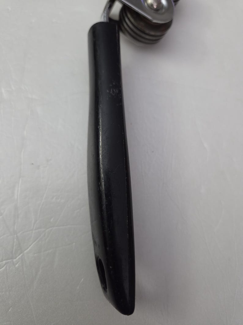 May include: A black can opener with a black handle and a silver, circular cutting mechanism. The handle is smooth and ergonomic, with a hole at the end for hanging. The can opener is designed for easy use.