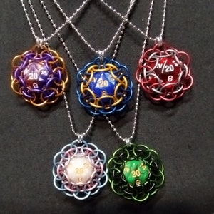 May include: Five silver chain necklaces with different colored metal d20 dice pendants. The dice are encased in a metal cage design. The dice are blue, green, pink, red, and purple.