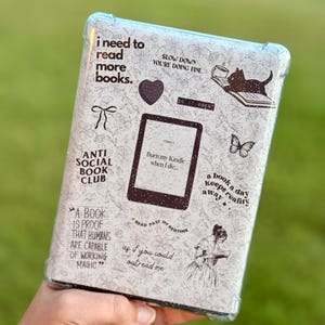 May include: A Kindle case with a floral pattern and various quotes and illustrations. The case features text that reads "I need to read more books," "Burn my Kindle when I die," and "A book a day keeps reality away."