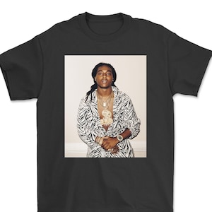 Puede incluir: Una camisa de manga larga con estampado en blanco y negro. La camisa tiene una cremallera y un cuello. La persona que lleva la camisa está de pie frente a una pared blanca.