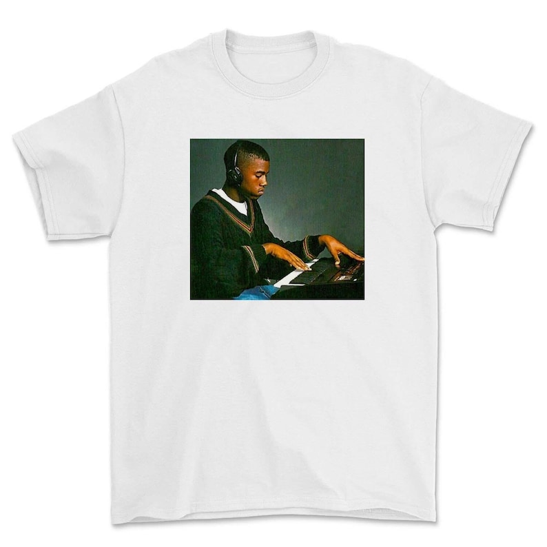 May include: A white t-shirt with a black and white image of a man wearing headphones and playing a keyboard.