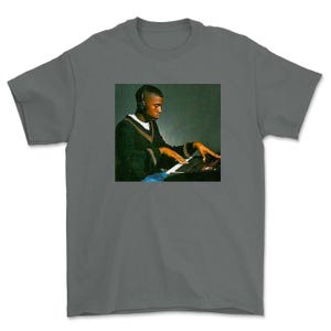 May include: A gray t-shirt with a black and white image of a man playing a keyboard.