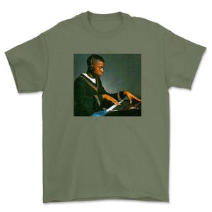 May include: A green t-shirt with a photo of a man wearing headphones and playing a keyboard.