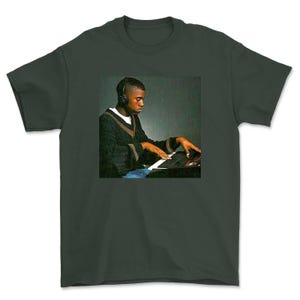 May include: A dark green t-shirt featuring a black and white photo of a man wearing headphones and playing a keyboard.