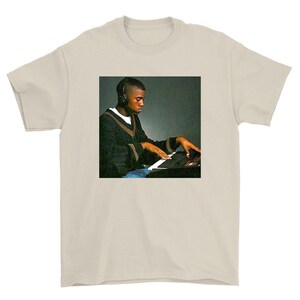 May include: A black and white photo of a person wearing headphones and playing a keyboard. The person is wearing a black sweater with a white collar and blue jeans.