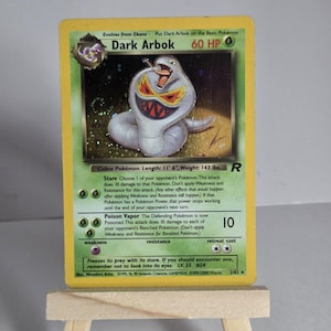 May include: A Dark Arbok Pokémon card with a cobra illustration. The card has a yellow border and green text boxes. The card text includes the Pokémon's HP, attacks, and abilities. The card is 11' 6" long and weighs 143 lbs.