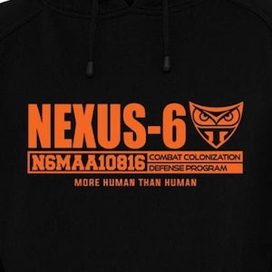 Puede incluir: Sudadera con capucha negra con una impresión naranja del texto "NEXUS-6" y "NGMAA10816 COMBAT COLONIZATION DEFENSE PROGRAM MORE HUMAN THAN HUMAN". La impresión también incluye un logotipo de búho estilizado.