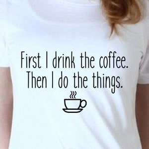 May include: White t-shirt with the text "First I drink the coffee. Then I do the things." and a small black and white illustration of a coffee cup with steam.