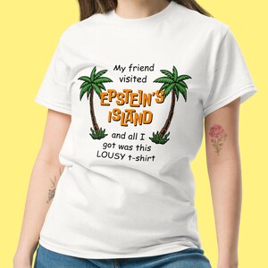 May include: White t-shirt with a graphic of palm trees and the text "My friend visited Epstein's Island and all I got was this lousy t-shirt."