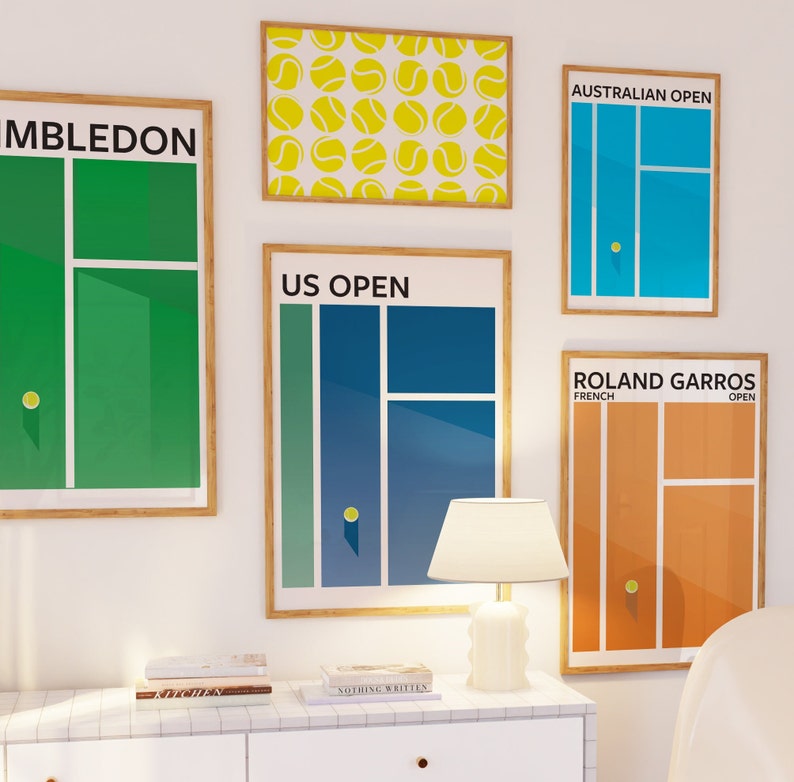 K&ouml;nnte beinhalten: Ein Satz von f&uuml;nf gerahmten Drucken mit verschiedenen Tennisplatzdesigns. Die Drucke sind mit den Namen der vier Grand-Slam-Turniere beschriftet: Wimbledon, US Open, Australian Open und Roland Garros. Die Drucke sind an einer wei&szlig;en Wand mit einem wei&szlig;en Tisch und einer Lampe davor angeordnet.