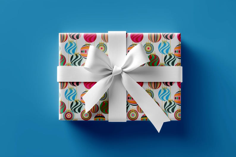 May include: A rectangular gift box wrapped in patterned paper featuring colorful Christmas ornaments. The box is tied with a white ribbon and bow, set against a solid blue background. The ornaments have stripes and swirls.