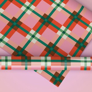 Könnte beinhalten: Rosa Geschenkpapier mit einem Karomuster in Rot, Grün und Braun. Ein aufgerollter Abschnitt des gleichen Papiers ist ebenfalls sichtbar, zusammen mit einem flachen Bogen. Der Hintergrund ist einfarbig rosa.