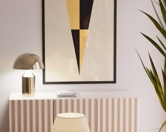 May include: A framed wall art print featuring a vertical pennant design divided into four alternating black and gold triangular sections. The artwork is displayed in a thin black frame against a plain wall, positioned above a textured sideboard.