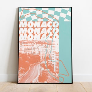 May include: A framed art print featuring a stylized aerial view of Monaco. The design incorporates a race track outline, a checkered flag, and the word "MONACO" in bold, stacked letters. The color palette includes shades of orange, teal, and white.