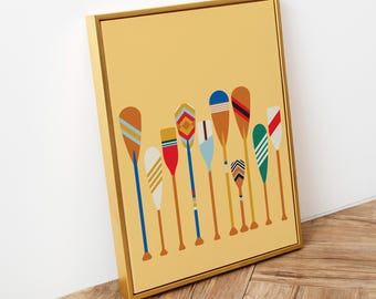 May include: A framed wall art print featuring a collection of ten colourful canoe paddles arranged vertically against a solid mustard yellow background. Each paddle displays a unique pattern of stripes, geometric shapes, and solid colour blocks.