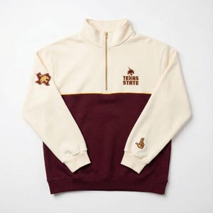 May include: Cream and maroon quarter-zip sweatshirt with gold zipper. Features the text "TEXAS STATE" and a logo on the chest, plus a Texas-shaped logo patch and a hand gesture patch on the sleeves. A casual, collegiate-style top.