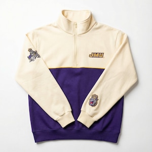May include: Cream and purple quarter-zip sweatshirt with the letters "JMU" in gold. The sweatshirt has a high collar and a gold stripe. Patches of a bulldog wearing a crown are on the sleeves.