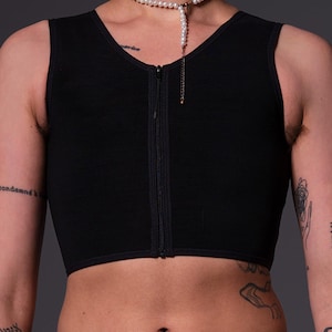 May include: A black sleeveless compression top with a front zipper closure. The top is cropped and has a smooth, matte finish.