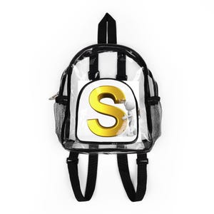 Op de afbeelding: Transparante rugzak met zwarte randen en bandjes. De rugzak heeft een witte vierkant met een gouden letter "S" en een klein wit figuur. De rugzak heeft een mesh zijvak en een ritssluiting.