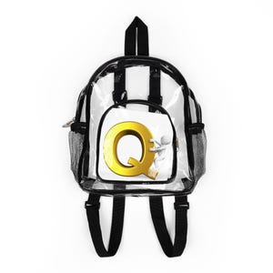 Op de afbeelding: Transparante rugzak met zwarte randen en banden. Een klein voorvak toont de gouden letter "Q" met een 3D-figuur. Het heeft een zijvak van gaas en een handvat aan de bovenkant. Eenvoudig en functioneel ontwerp.